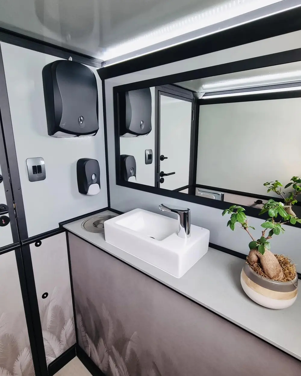 Restroom trailer vanity with sink, mirror and dispensers