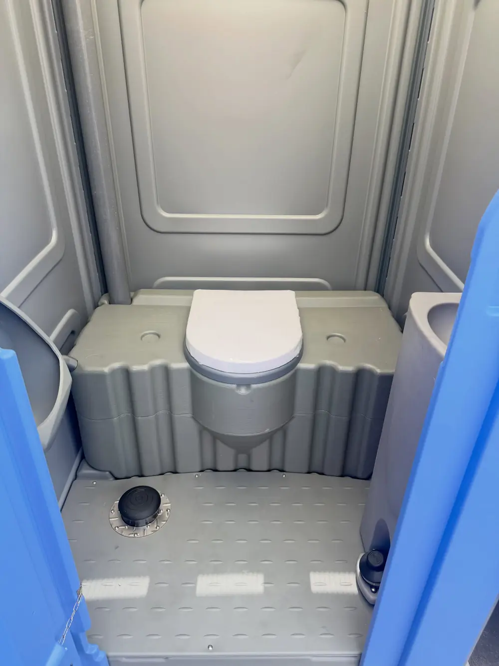 Two blue standard porta potties on pavement
